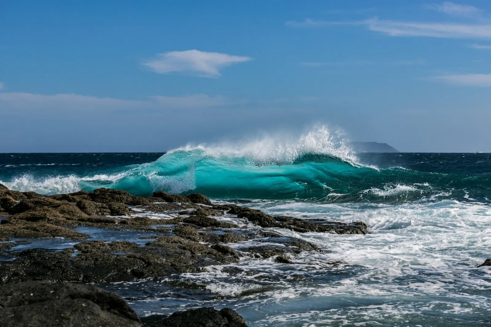 Turquoise wave breaking over black lava rock on the Hawaiʻi Island coast